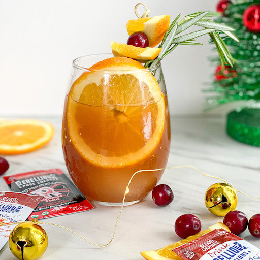 Antioxidant Orange Infusion Mocktail in Glass on Table with Fruit Christams Decorations and Liquid Packets of Rebellious Infusions Courageous (Cherry with Guava) and Blood Orange