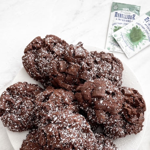 Mint Chocolate Chunk Cookies Made with Rebellious Infusions on white plate on white marble countertop with liquid packets of Rebelllious Infusions and silver garland.